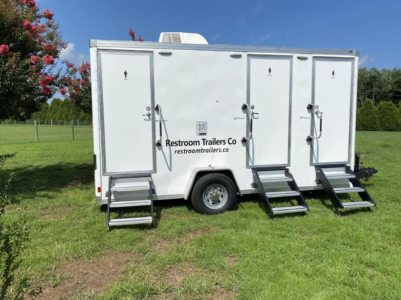 Three station luxury restroom trailer set up on grass with steps down