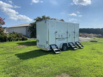 Rear of the restroom trailer showing the roof air conditioning unit and three entry doors with steps down