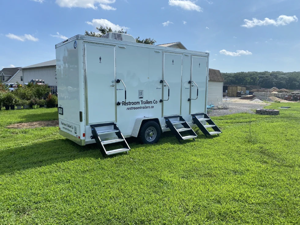 Three-station restroom trailer with all doors closed and steps down, a materials yard and gravel behind it