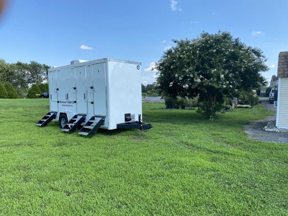 Restroom trailer set up on an open lawn with trees and a house in the background