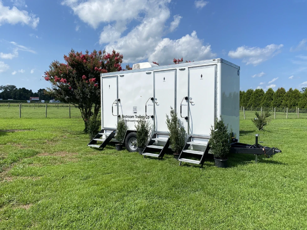 Side view of the restroom trailer parked on grass beside a flowering crepe myrtle