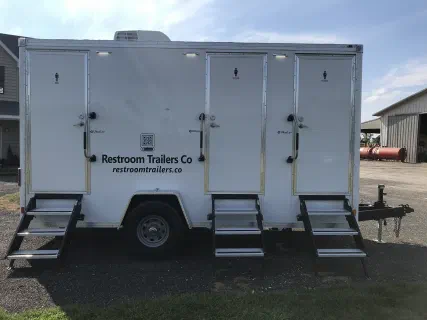 Restroom trailer parked on a gravel lot with all four doors and steps in place
