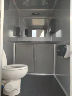 Inside a private stall with a flushing toilet, vinyl floor, and overhead lighting