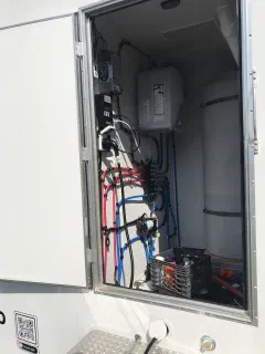 Open utility compartment showing the fresh water tank, water pump, water heater, and electrical panel