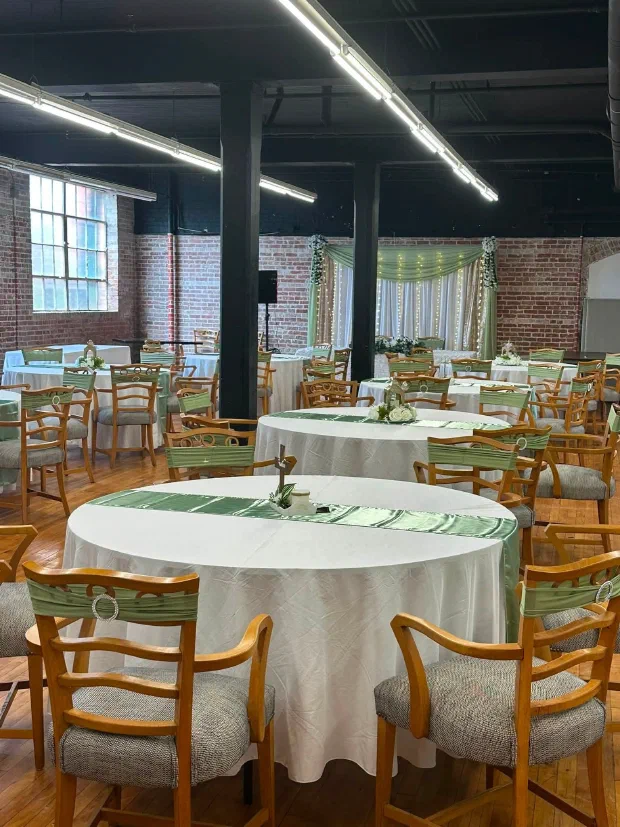 Wedding reception at Pleasant Street Hall in Cambridge, MD, with round tables and sage green linens under brick walls and black beams